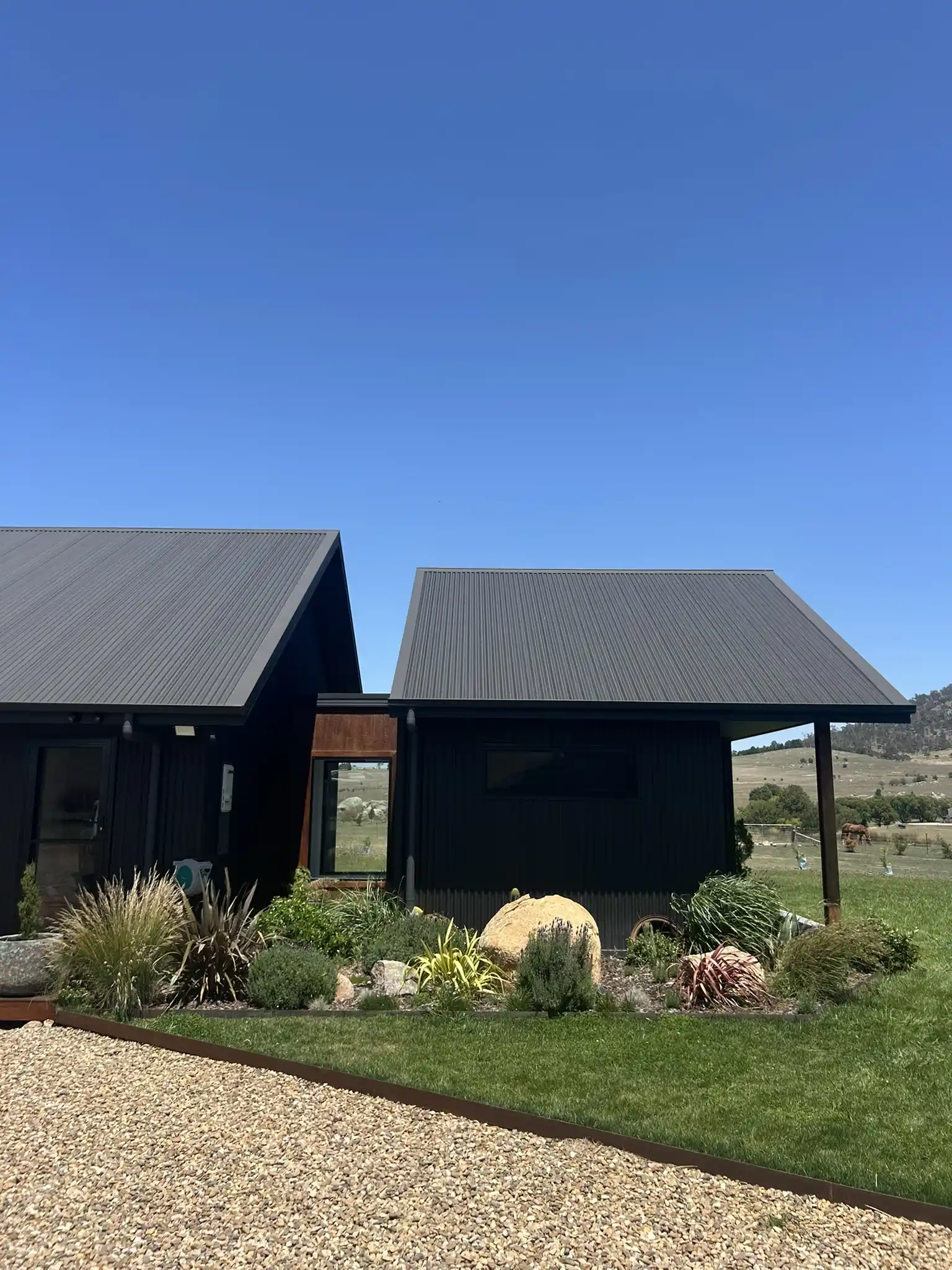 Black timber house with native planting, boulders, lawn and gravel